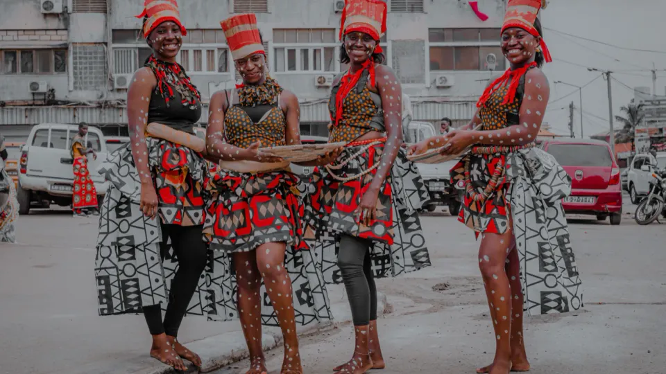Quatro dançarinas com trajes tradicionais angolanos numa rua de Luanda.