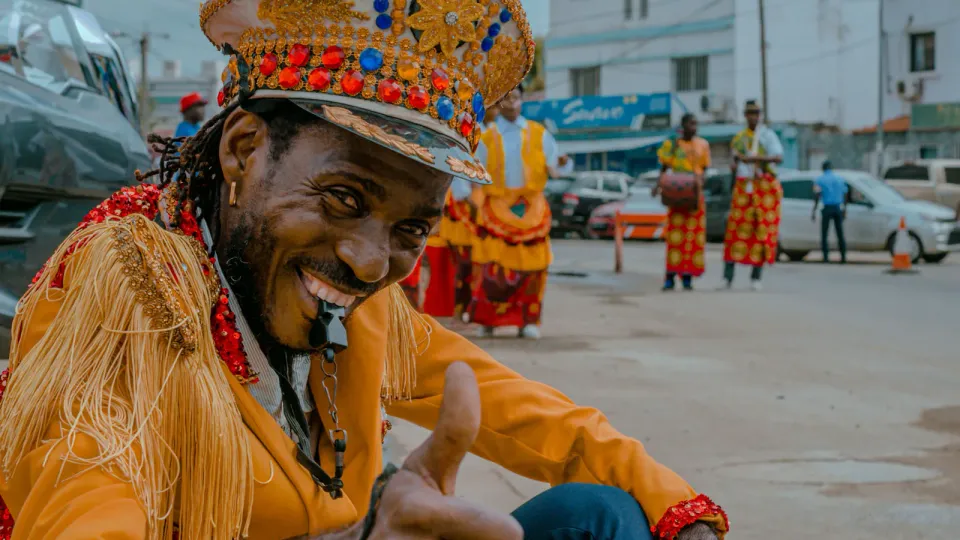 Figurante do carnaval de Luanda, com traje e chapéu tradicionais, a sorrir e a fazer sinal de aprovação.