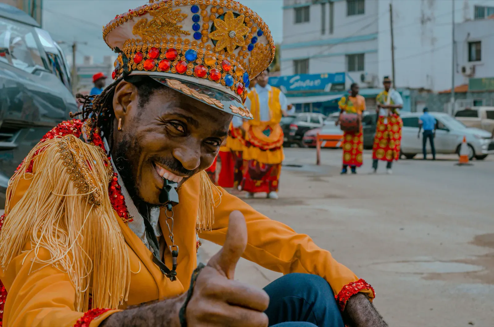 Figurante do carnaval de Luanda, com traje e chapéu tradicionais, a sorrir e a fazer sinal de aprovação.
