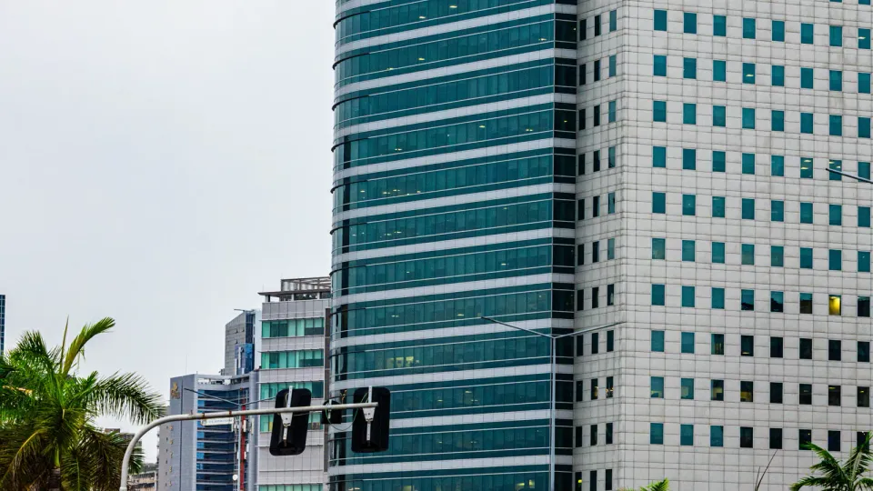 Avenida moderna de Luanda com torres de escritórios, palmeiras e trânsito.