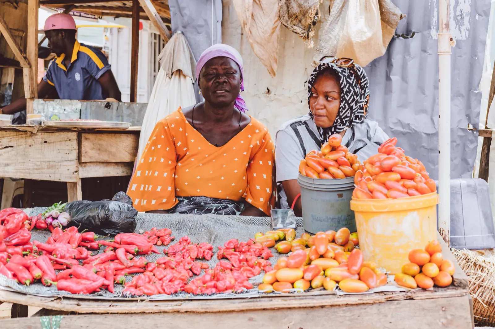 Duas vendedoras numa banca de mercado com tomate e pimento frescos.