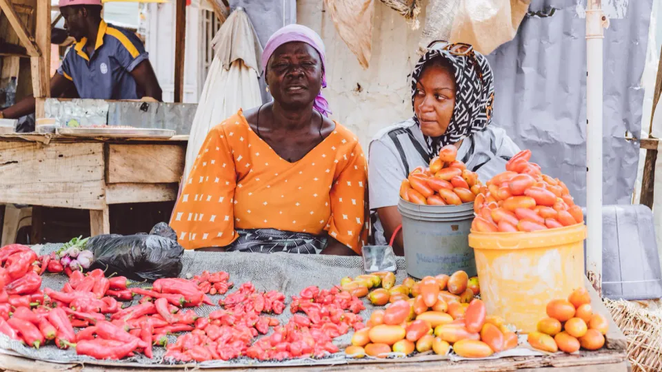 Duas vendedoras numa banca de mercado com tomate e pimento frescos.