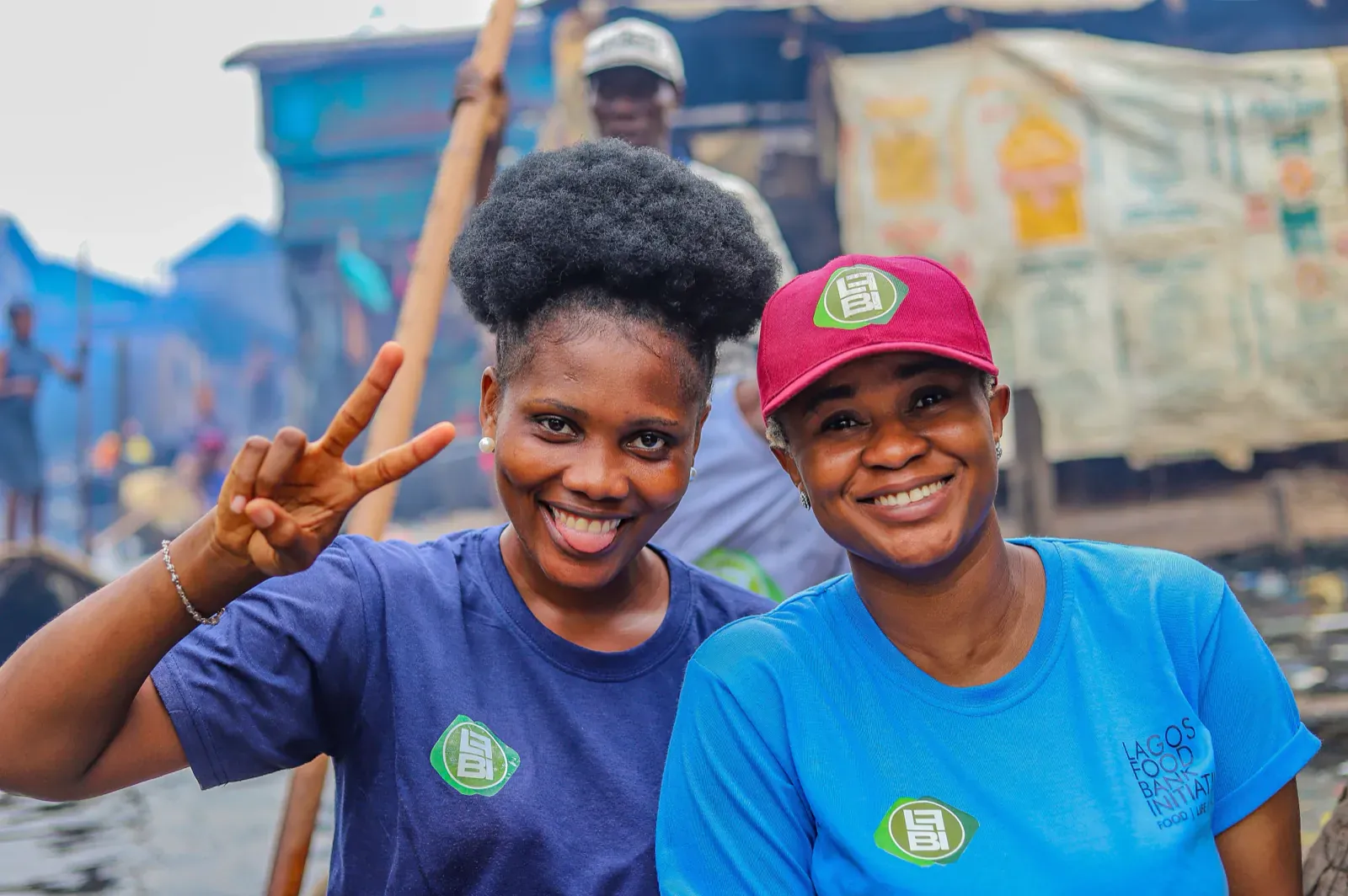 Duas voluntárias a sorrir durante uma acção comunitária, uma delas a fazer o sinal de vitória.